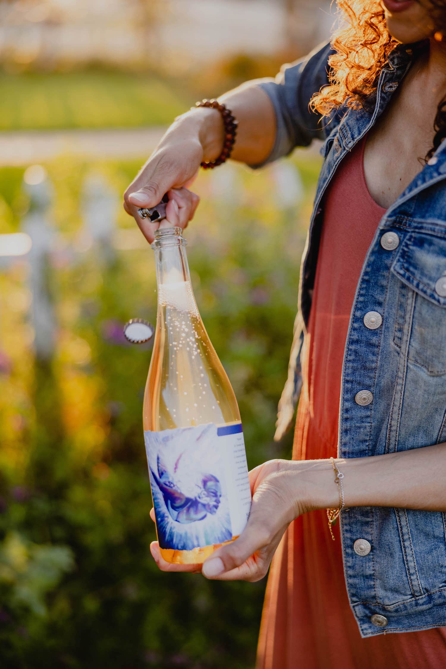 Person holding and opening a bottle of sparkling wine in a garden setting