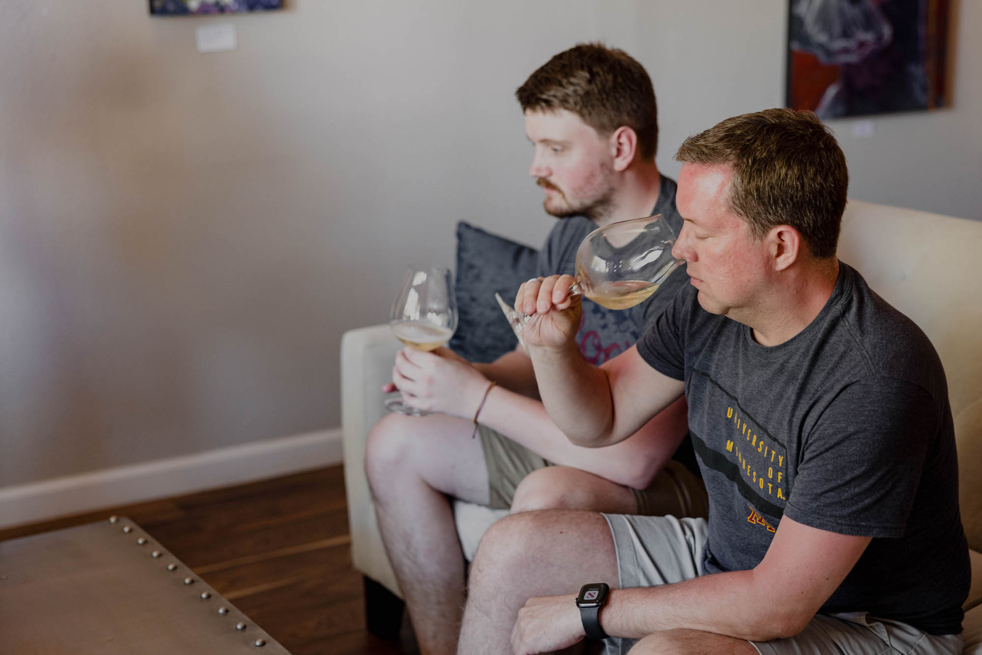 Two men drinking Chardonnay wine on a couch in a wine tasting room